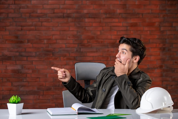 Vista frontal ingeniero masculino sentado detrás de su lugar de trabajo trabajo contratista de negocios agenda documento plan de propiedad corporativa