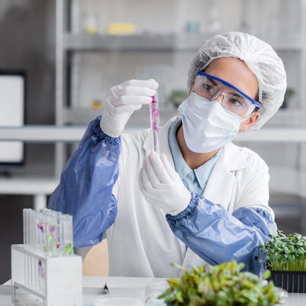 Vista frontal del investigador con tubo de ensayo y planta en el laboratorio de biotecnología