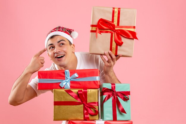 Vista frontal del joven alrededor de diferentes regalos de Navidad en la pared rosa