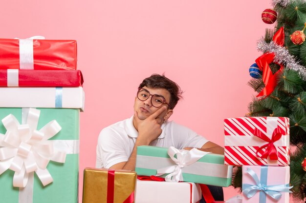 Vista frontal del joven alrededor de regalos y árbol de Navidad en la pared rosa