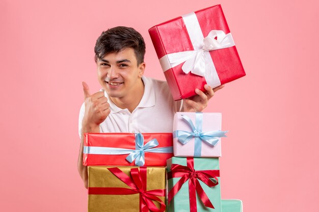 Vista frontal del joven alrededor de regalos de Navidad en la pared rosa