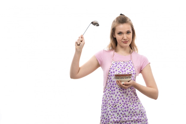 Una vista frontal joven ama de casa hermosa en camisa rosa colorida capa con plato y cuchara de plata sonriendo