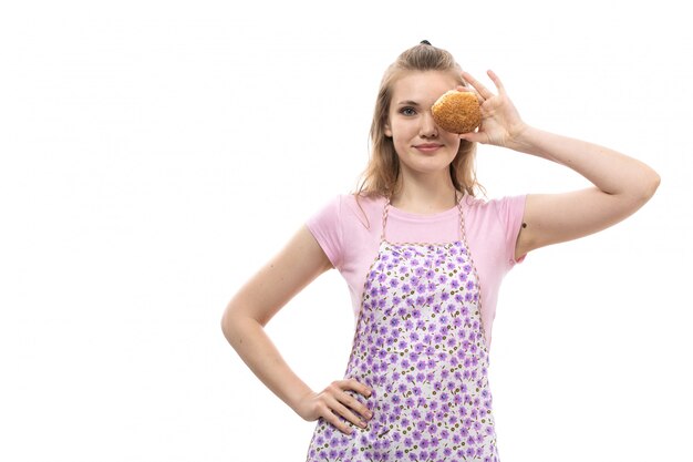 Una vista frontal joven ama de casa hermosa en camisa rosa colorida capa sosteniendo y cubriendo su ojo con poco pan sonriendo