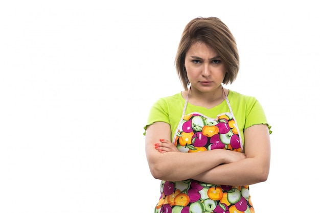 Una vista frontal joven ama de casa hermosa en camisa verde capa colorida posando expresión enojada disgustado en el fondo blanco casa cocina femenina