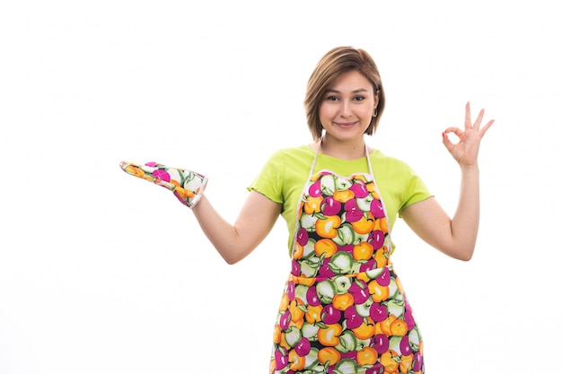 Una vista frontal joven ama de casa hermosa en camisa verde capa colorida posando sonriente sobre el fondo blanco limpieza de la casa cocina