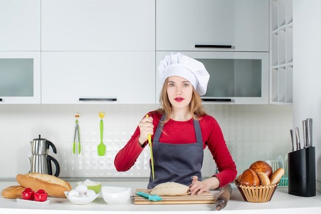 Vista frontal joven ama de casa con sombrero de cocinero y delantal cortando pan en la cocina