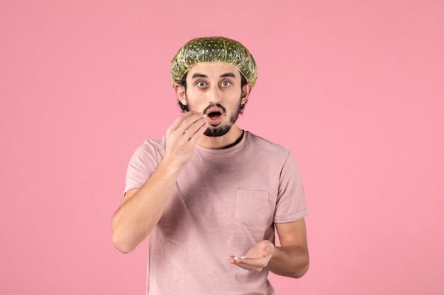 Vista frontal del joven aplicando máscara en su rostro en la pared rosa