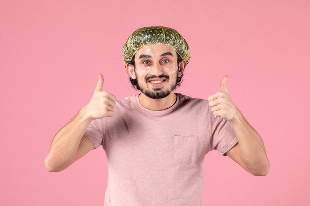 Vista frontal del joven aplicando máscara en su rostro en la pared rosa