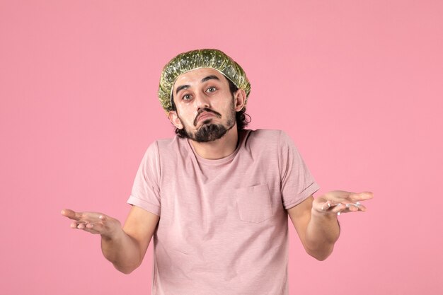 Vista frontal del joven aplicando máscara en su rostro en la pared rosa