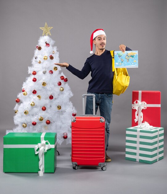 Vista frontal joven apuntando con el dedo que muestra el árbol de Navidad en aislado