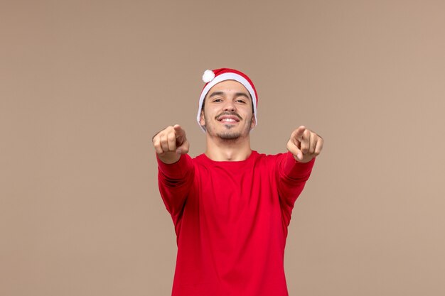 Vista frontal joven apuntando con una sonrisa sobre fondo marrón color masculino emoción vacaciones