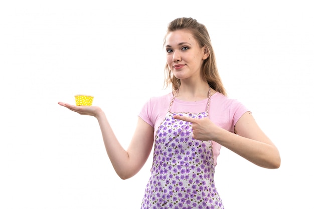 Una vista frontal joven y atractiva ama de casa en camisa rosa capa colorida celebración amarillo cosa sonriente sobre el fondo blanco cocina cocina femenina