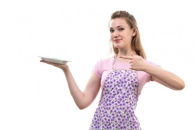 Una vista frontal joven y atractiva ama de casa en camisa rosa colorida capa con plato blanco sonriendo posando sobre el fondo blanco cocina cocina femenina