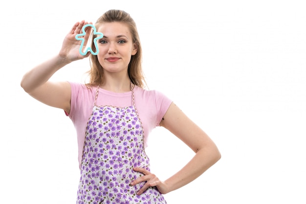 Una vista frontal joven y atractiva ama de casa en camisa rosa colorida capa posando sonriendo sosteniendo poco azul humano formado juguete sobre el fondo blanco cocina cocina femenina