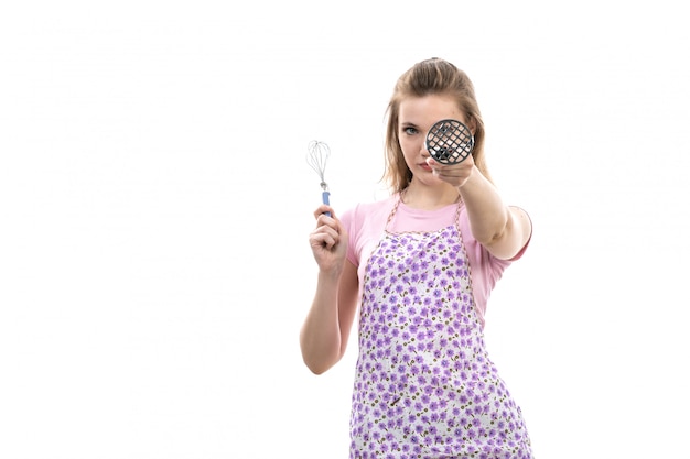 Una vista frontal joven y atractiva ama de casa en camisa rosa colorida capa posando sonriente sosteniendo algo sobre el fondo blanco cocina cocina femenina