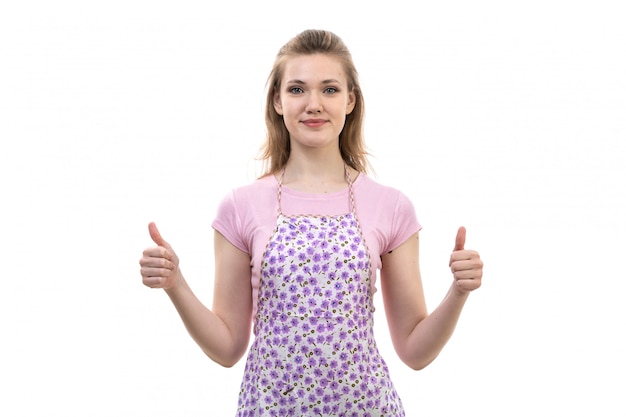 Una vista frontal joven y atractiva ama de casa en camisa rosa colorida capa sonriendo posando mostrando impresionantes dedos de expresión en el fondo blanco cocina cocina femenina