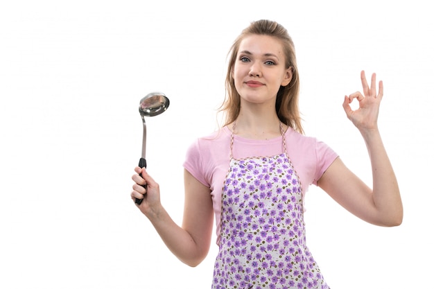 Una vista frontal joven y atractiva ama de casa en camisa rosa colorida capa sonriendo posando sosteniendo electrodomésticos en el fondo blanco cocina cocina femenina