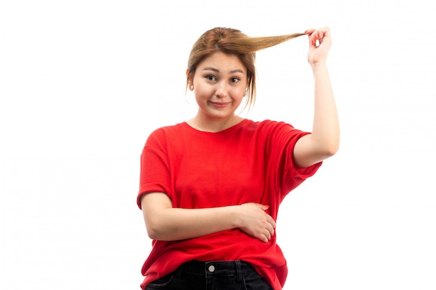 Una vista frontal joven atractiva en camiseta roja con jeans negros tirando de su cabello en el blanco