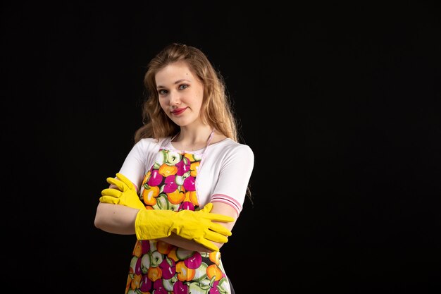 Una vista frontal joven y atractiva chica en capa colorida sonriendo con guantes amarillos sobre el fondo negro amor sonrisa positividad