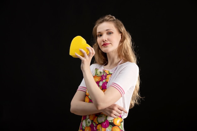 Una vista frontal joven y atractiva chica en capa colorida sonriendo sosteniendo forma de corazón amarillo sobre fondo negro amor sonrisa positividad