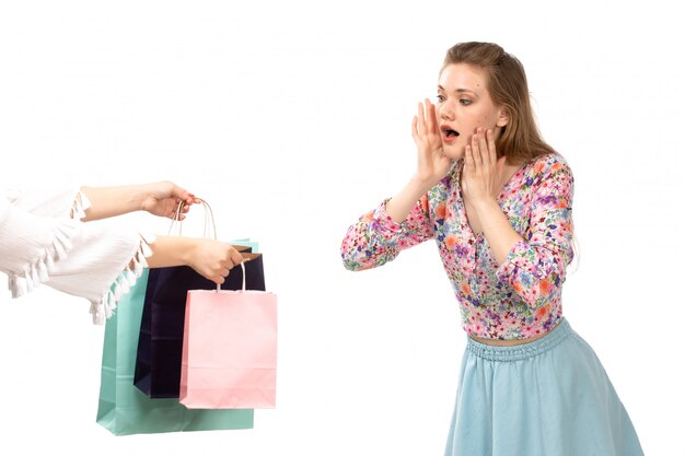 Una vista frontal joven y atractiva dama en camisa colorida flor diseñada y falda azul obteniendo paquetes de compras en el blanco