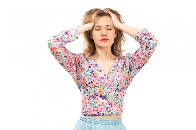 Una vista frontal joven y atractiva dama en camisa colorida flor diseñada y falda azul posando con los ojos cerrados en el blanco