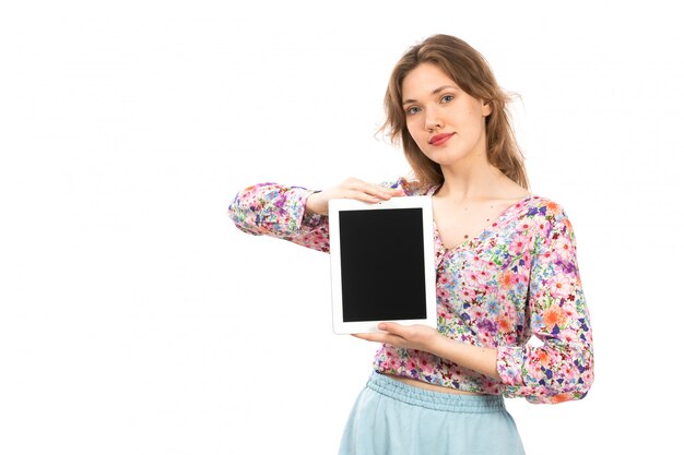 Una vista frontal joven y atractiva dama en camisa colorida flor diseñada y falda azul con tableta blanca sobre el blanco