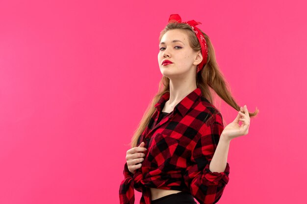 Una vista frontal joven y atractiva dama en camisa a cuadros rojo-negro pantalón negro posando sobre el fondo rosa moda femenina joven