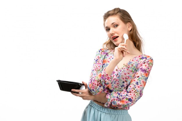 Una vista frontal joven y atractiva dama en camisa de diseño colorido y falda azul con cuenco negro posando en el blanco