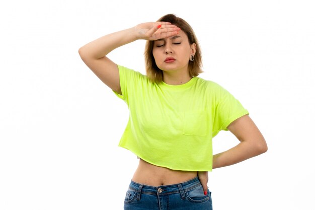 Una vista frontal joven y atractiva dama en camisa verde y jeans azul que sufren de alta temperatura en el blanco