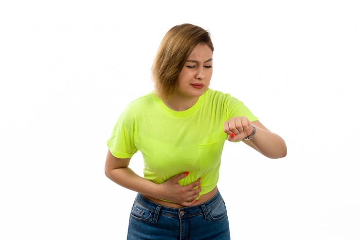 Foto gratuito una vista frontal joven y atractiva dama en camisa verde y jeans azul que sufren de dolor de estómago mirando su reloj en el blanco