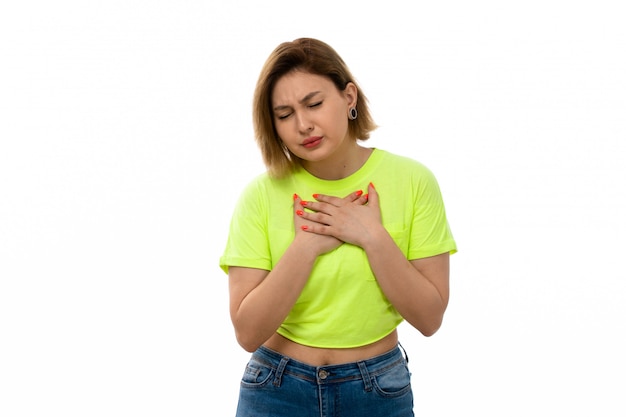 Una vista frontal joven y atractiva dama en camisa verde y jeans azul que sufren problemas de respiración en el blanco