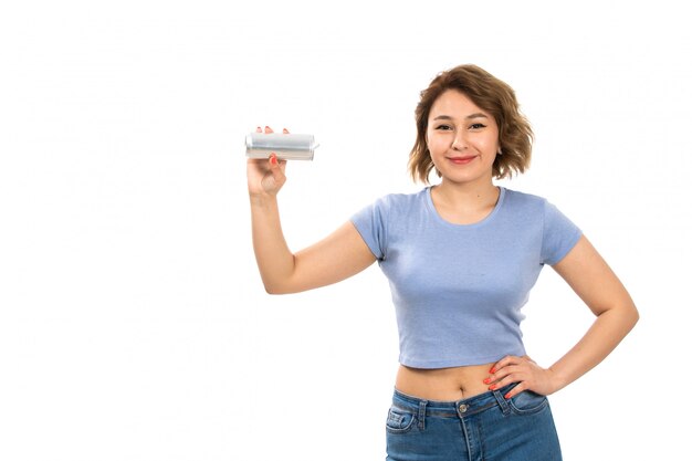 Una vista frontal joven y atractiva dama en camiseta gris y jeans azul con plata puede sonriendo en el blanco