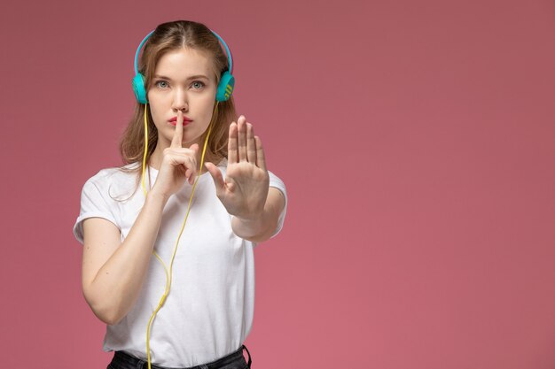 Vista frontal joven atractiva mujer escuchando música a través de sus auriculares mostrando el signo de silencio en la pared rosa modelo color mujer joven