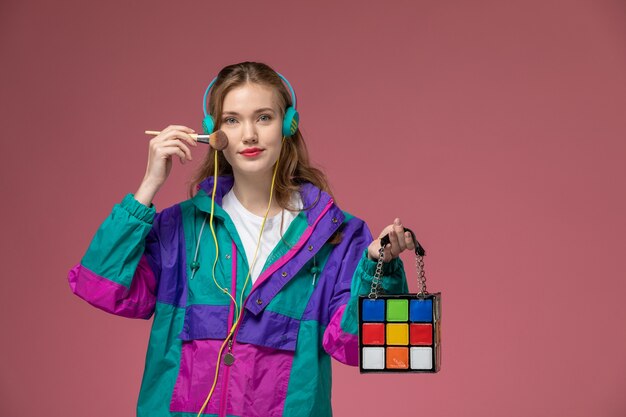 Vista frontal joven atractiva mujer vistiendo abrigo de color escuchando música sonriendo en la pared de color rosa oscuro modelo color mujer joven