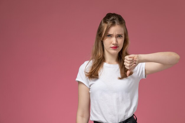 Vista frontal joven atractiva mujer vistiendo una camiseta blanca que muestra signo diferente en la pared de color rosa oscuro modelo color mujer joven