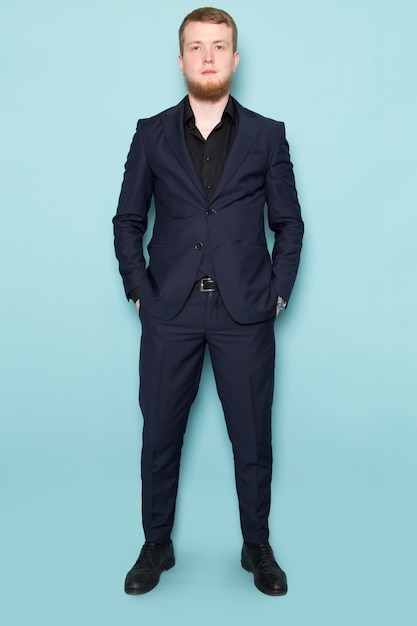 Una vista frontal joven atractivo hombre con barba en negro oscuro clásico traje moderno en el espacio azul