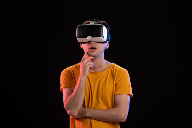 Vista frontal del joven con auriculares vr en la pared oscura