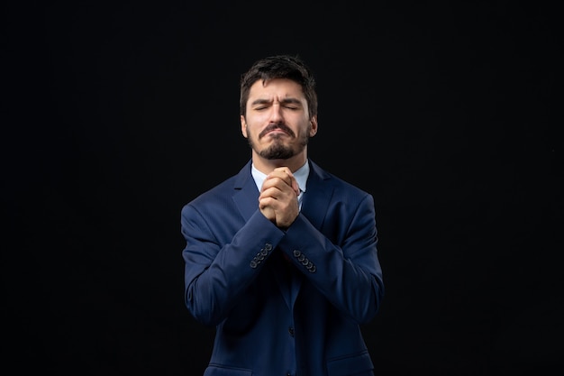 Foto gratuita vista frontal del joven barbudo esperanzado orando por dios en la pared oscura aislada