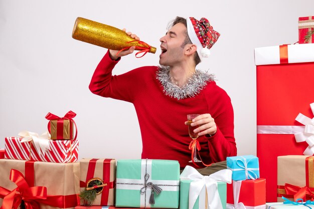 Vista frontal joven bebiendo champán sentados alrededor de regalos de Navidad