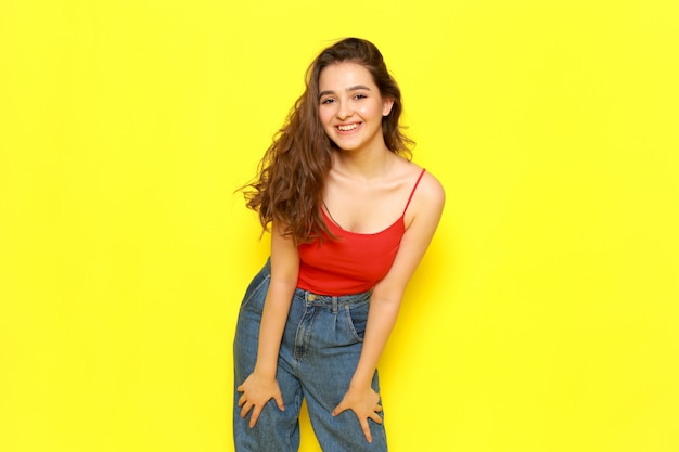 Una vista frontal joven y bella chica en camisa roja y jeans azul simplemente posando con expresión feliz