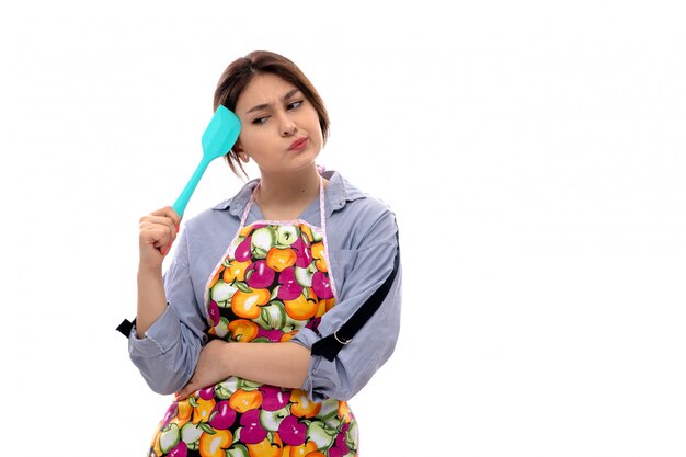 Una vista frontal joven y bella dama en camisa azul claro y capa colorida pensando sosteniendo electrodomésticos de cocina azul