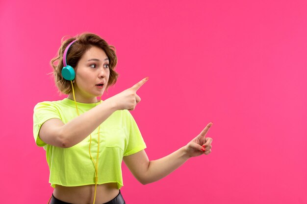 Una vista frontal joven bella dama en camisa de color ácido pantalón negro con auriculares azules escuchando música