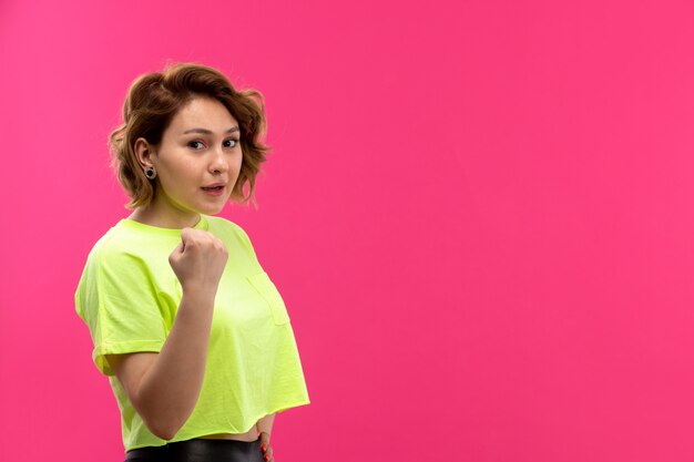 Una vista frontal joven y bella dama en camisa de color ácido pantalón negro posando feliz