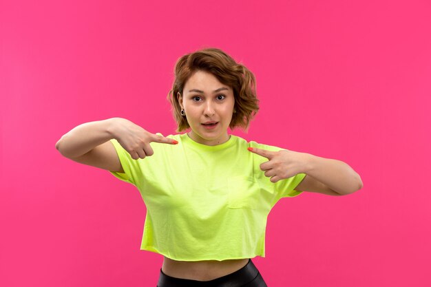 Una vista frontal joven bella dama en camisa de color ácido pantalón negro posando