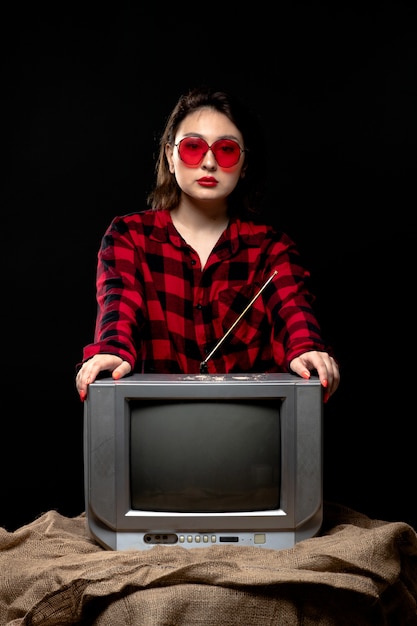 Foto gratuita una vista frontal joven bella dama en camisa a cuadros rojo-negro en gafas de sol rojas cerca de little tv