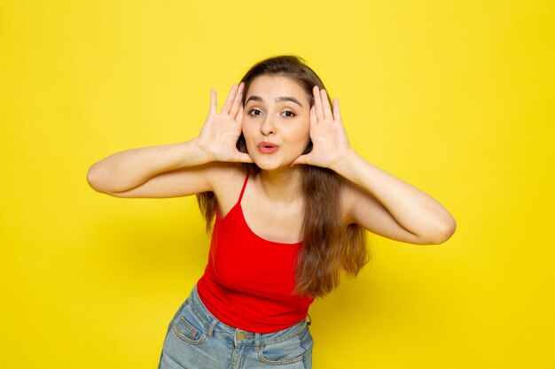 Una vista frontal joven bella dama en camisa roja y blue jeans posando cara