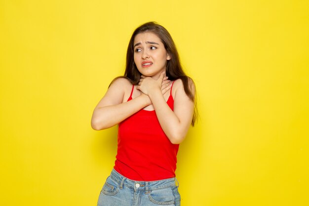 Una vista frontal joven y bella dama en camisa roja y jeans azul calzándose