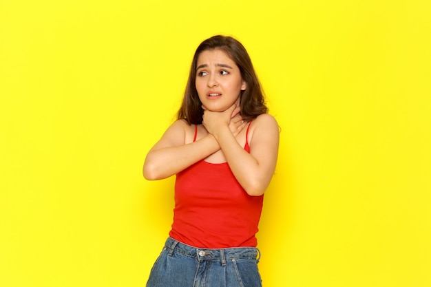 Una vista frontal joven y bella dama en camisa roja y jeans azul calzándose