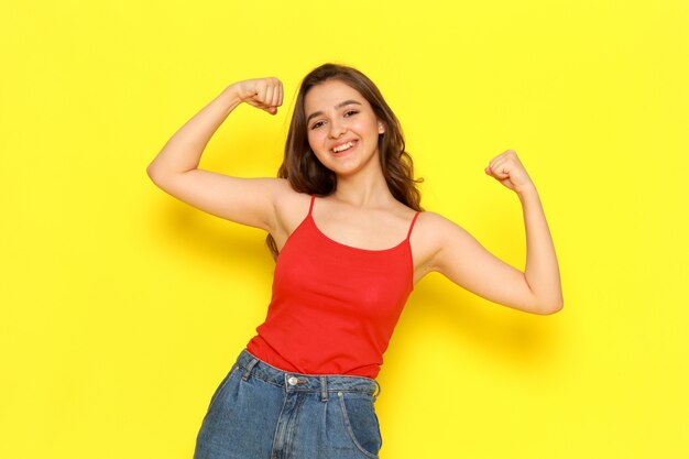 Una vista frontal joven y bella dama en camisa roja y jeans azul flexionando y sonriendo